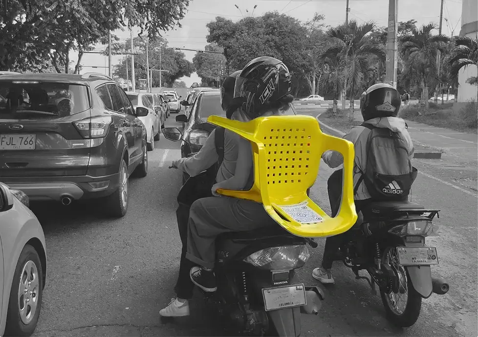 Un parrillero lleva una silla Rimax amarilla en moto, entre el tráfico